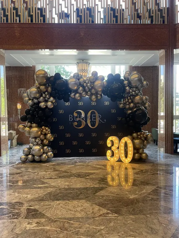 Black, silver and gold balloon arch with a custom backdrop in a hotel lobby